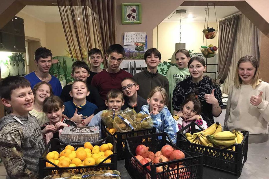 De kinderen van het kinderhuis staan in de keuken met kratten vers fruit.